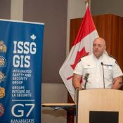 Male police officer stands behind a podium in front of a Canadian flag and G7 display signage.