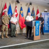 Six men in uniform from difference law enforcement and defence agencies stand behind a podium during a press conference.