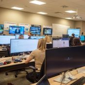 Open office space where large group works behind computer screens displaying news coverage.