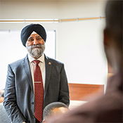 Senator Dhillon wearing a suit and turban stands at the front of a classroom speaking to RCMP DICE participants.
