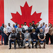 A group of participants and staff pose for a group photo in the Drill Hall of the RCMP Training Academy at Depot.