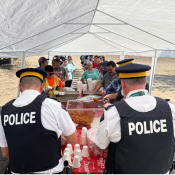 Police officers serve food and drinks under a white canopy to people lined up at an outdoor event.