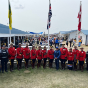 RCMP officers in a red serge uniform stand in front of flags at an outdoor gathering.