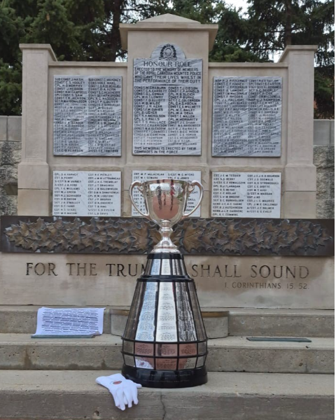 A silver trophy and a small white blanket are set in front of a stone and marble memorial listing the Mounties who died in the line of duty.