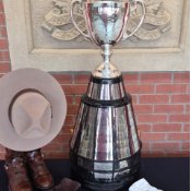 A trophy stands on a short table with a small white blanket. Next to it are an RCMP Stetson resting atop a pair of RCMP boots.