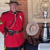 An RCMP officer in red serge and a man in a dark suit stand either side of a silver trophy.