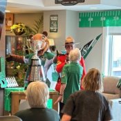 An RCMP officer in a red uniform shows off a silver trophy to a room of elderly men and women.