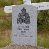 A gray headstone bearing the RCMP crest and Special Constable Peter Esau's name, regimental number, birth date and date of his death atop a grave amid a field of crosses.