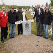 9 people stand at a grave marked with an RCMP headstone and a cross amid a graveyard filled with crosses.