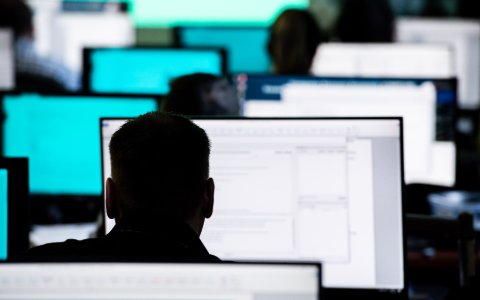 Silhouetted figures sit in front of rows of computer screens