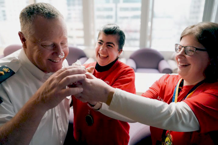 Two women feed a donut to an RCMP officer in a white shirt