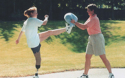 Retired RCMP member Laurie White during her rehabilitation with a prosthetic leg, kicking a pad someone is holding. 