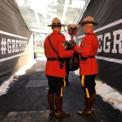 Two officers in Red Serge carry the Grey Cup onto a football field