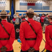 Three officers in Red Serge are gathered with high school students admiring the Grey Cup.