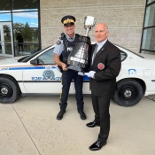 Two men hold the Grey Cup trophy in front of a police cruiser