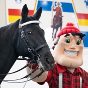 A lumberjack mascot pets a black horse