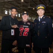 Former footballer shows championship ring as he stands beside an officer in uniform and man wearing REDBLACKS jersey.