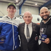 Two Winnipeg Blue Bombers pose with the Keeper of the Cup in front of an RCMP plane.