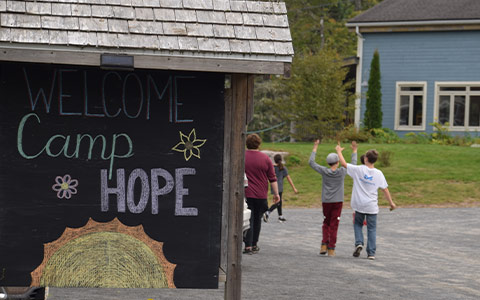 Unidentifiable children play in the background of a sign that reads: Welcome to Camp Hope.