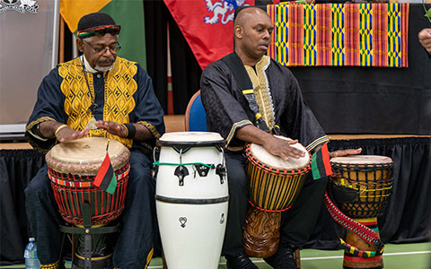 Two people drum as they sit in front of a stage.