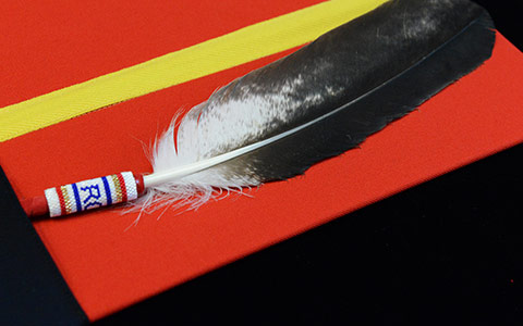 An eagle feather sits on a red folder that has a yellow ribbon around it.