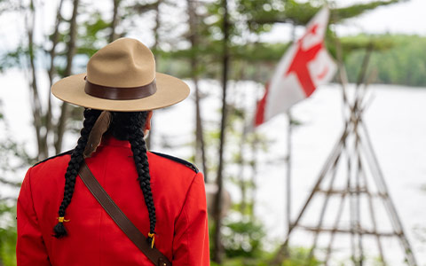 An RCMP officer in red serge, with their back to the camera, looks at a Grand Council Flag of the Mi’kmaq Nation.