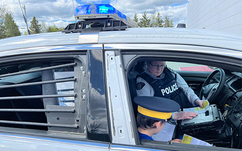 An RCMP officer and an unidentifiable child sitting in a police car looking at documents.