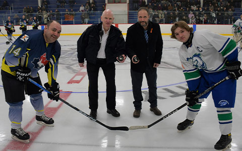 Two hockey players and two officials smile at the camera before the puck drops.