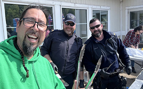 Two police officers and a community member smile at the camera as they stand behind a barbecue.