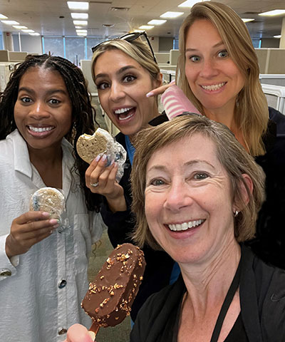 Four women hold ice cream and smile at the camera inside an office 
