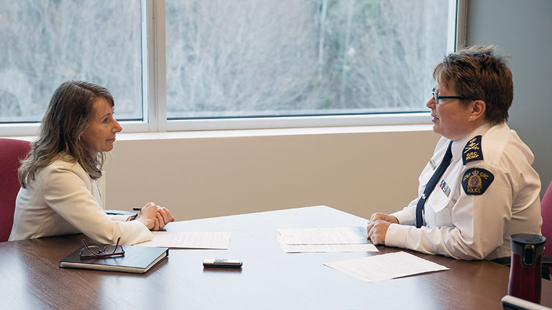 Two women, one in an RCMP uniform, sit at a table talking.
