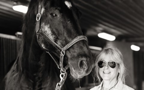 Saddled young rider embraces older black horse.