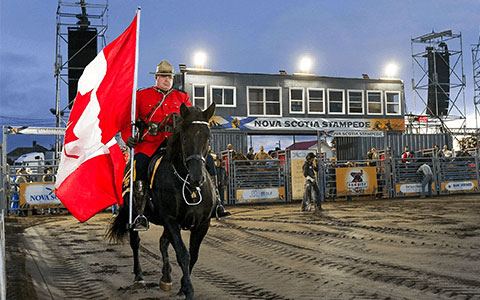 An RCMP officer in red serge riding a horse and carrying the Canadian flag.