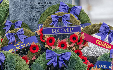 Memorial wreaths, including one with an RCMP ribbon, sitting in front of a cenotaph.