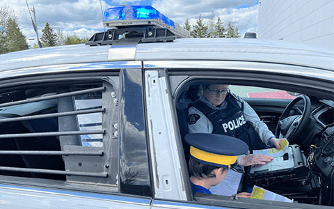 An RCMP officer and an unidentifiable child sitting in a police car looking at documents.