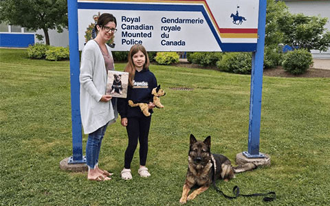 A woman and child standing in front of an RCMP sign, with a police dog on the ground beside them.
