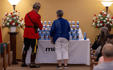 An RCMP officer in red serge and a member of the public light candles that are sitting on a table.
