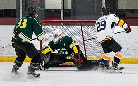 Two players from opposing teams skate up to a goalie in net.