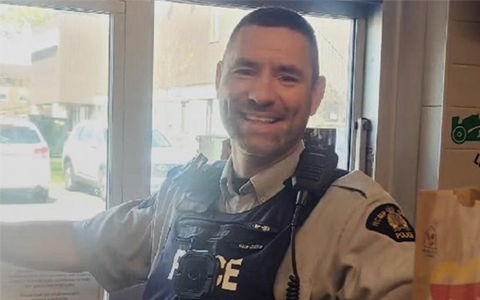 An RCMP officer smiles at the camera while standing at a McDonald’s drive-thru.