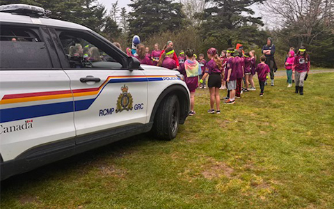 Several students stand on a field in front of an RCMP vehicle.
