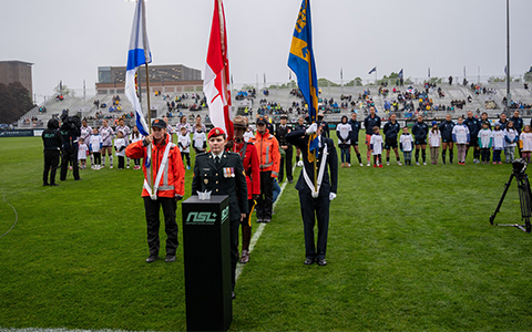 Female flag-bearers stand on a field in front of a podium.