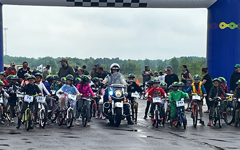 An RCMP officer on a motorcycle sits amidst cyclists at the start line of a race.