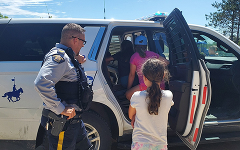 An RCMP officer looks on as children check on his police vehicle.
