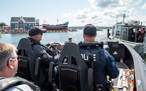 RCMP officers sit in a patrol boat; the ship Hector is seen in the background.