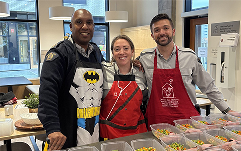 RCMP officers in aprons stand in front of food they prepped.