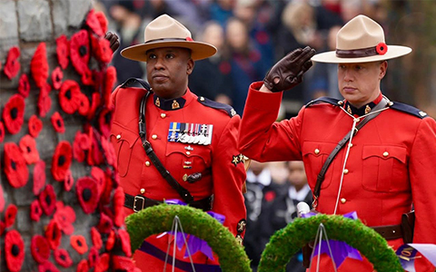 Two RCMP officers in red serge salute at a Remembrance Day ceremony.
