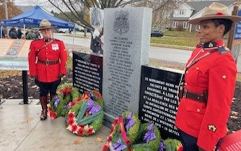 Two RCMP officers in red serge stand in front of a monument.