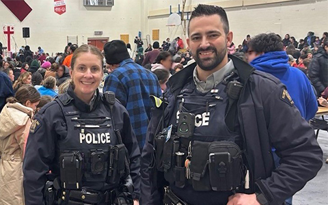 Two RCMP officers pose for a photo with a crowd pictured behind them.