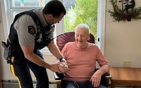 An RCMP officer talks with a resident sitting in a chair.