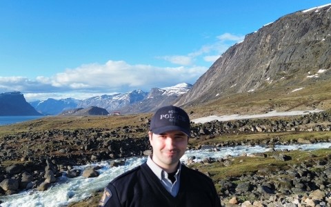 Man wearing RCMP police cap smiles at the camera with snow capped mountains in the landscape.